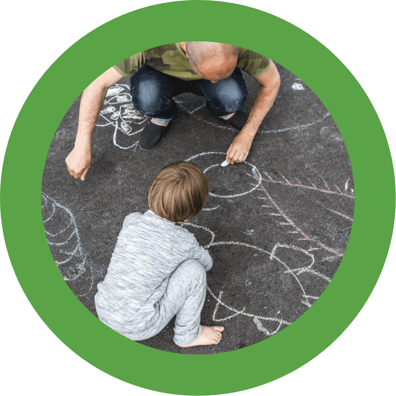 A man and his son drawing on the sidewalk with chalk.